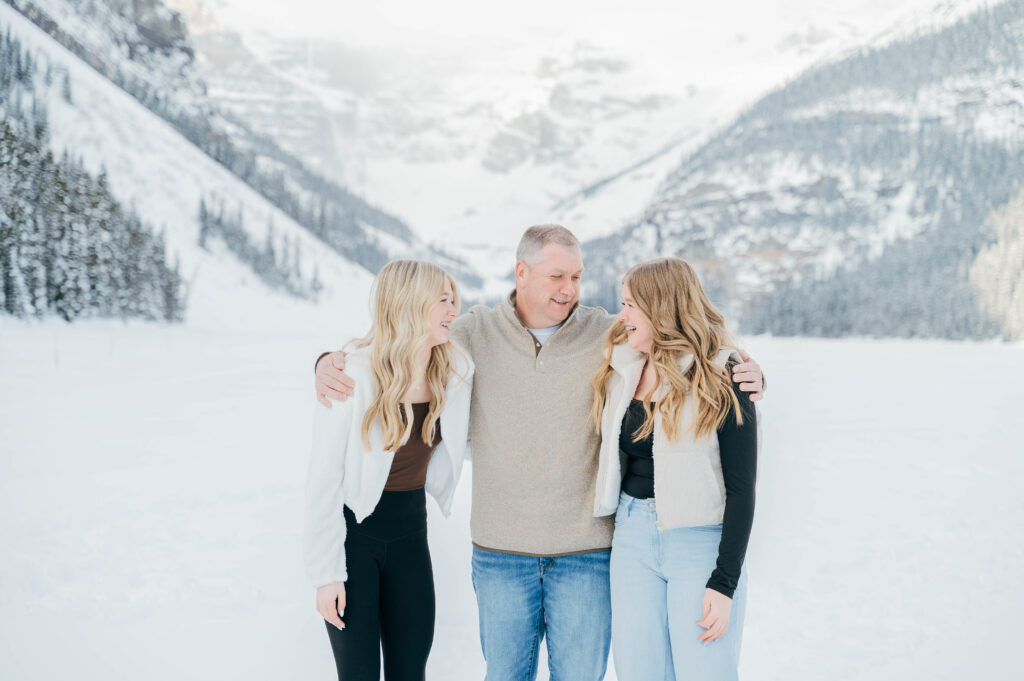 Two daughters and father hugging and laughing while posing for a photo in Lake Louise