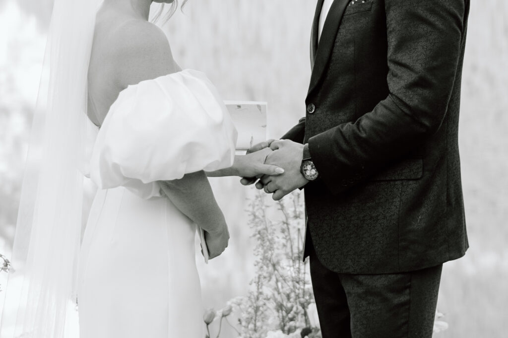 black-and-white-detail-of-couple-holding-hands-during-styled-lake-louise-wedding-ceremony-banff-wedding-photography