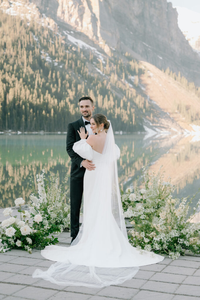 bride-and-groom-posing-during-styled-lake-louise-wedding-with-mountain-reflection-and-white-floral-arches-banff-wedding-photography