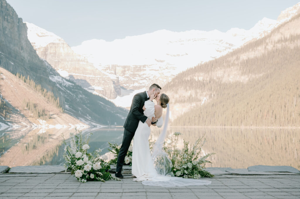 bride-and-groom-kissing-during-styled-lake-louise-wedding-with-mountain-backdrop-and-white-floral-arches-lake-louise-wedding-photography