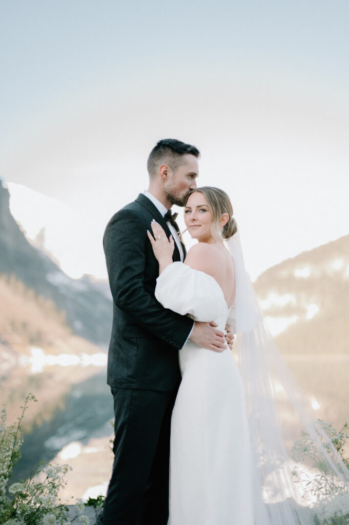 groom-kissing-bride-on-forehead-during-styled-lake-louise-wedding-with-mountain-backdrop-banff-wedding-photography