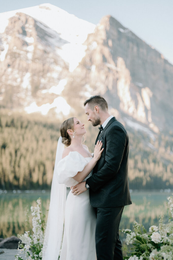 bride-and-groom-embracing-during-styled-lake-louise-wedding-with-mountain-backdrop-and-white-florals-banff-wedding-photography