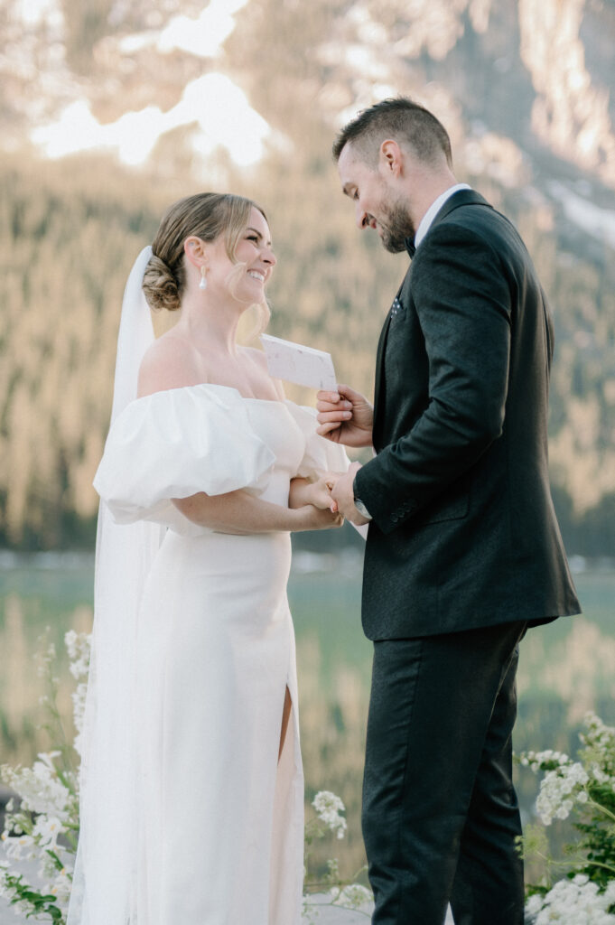 bride-and-groom-exchanging-vows-at-styled-lake-louise-wedding-with-mountain-backdrop-and-white-florals-lake-louise-wedding-photography
